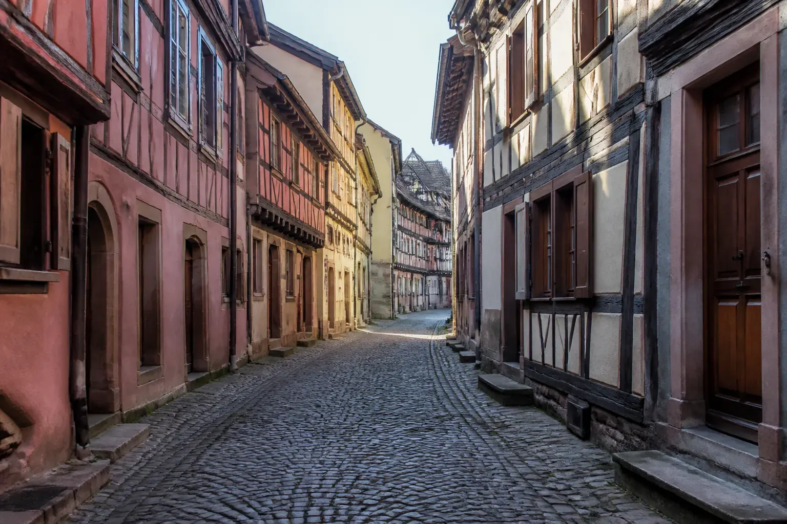 Ruelle alsacienne pavée bordée de maisons à colombage anciennes, façades colorées
